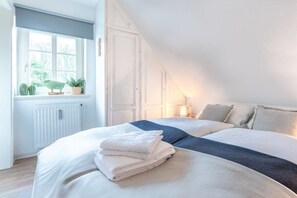 A bedroom with a bed, a window with plants, and a radiator. - Holiday apartment with 1 bedroom (Wyk auf Föhr)
