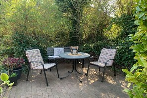 An outdoor patio with a round table and two chairs, surrounded by dense foliage. - Holiday apartment with 1 bedroom (Wyk auf Föhr)