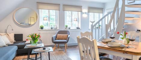 A modern living room with a sofa, a dining table set for two, a staircase, and a large mirror.