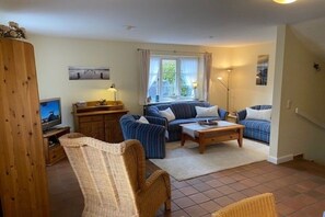 A living room with a television, sofa, armchair, and a window with curtains. - 8b in the building on Neuer Weg (Wrixum)