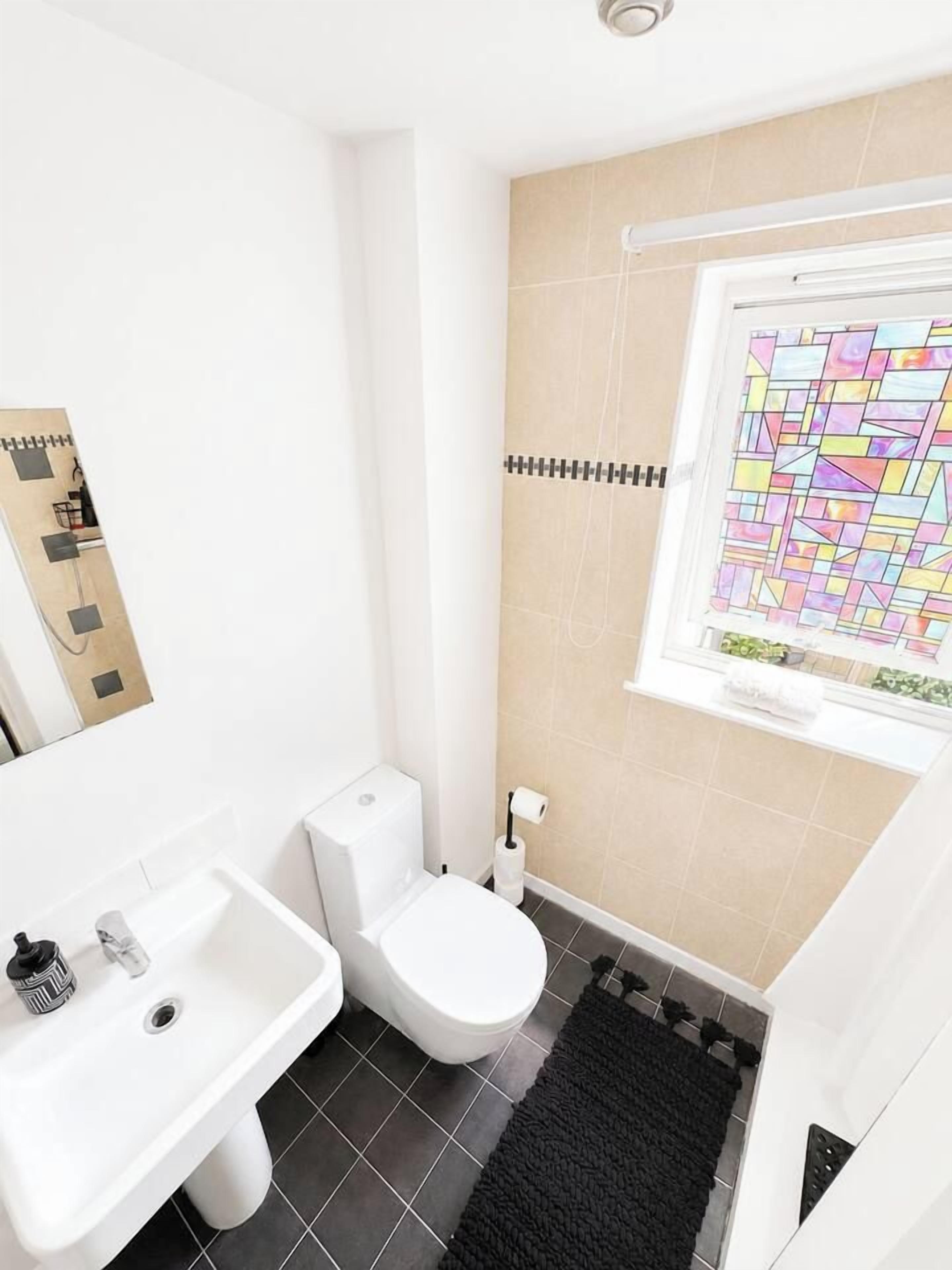Een compacte badkamer met toilet, wastafel en een raam met een glas-in-lood ontwerp.
