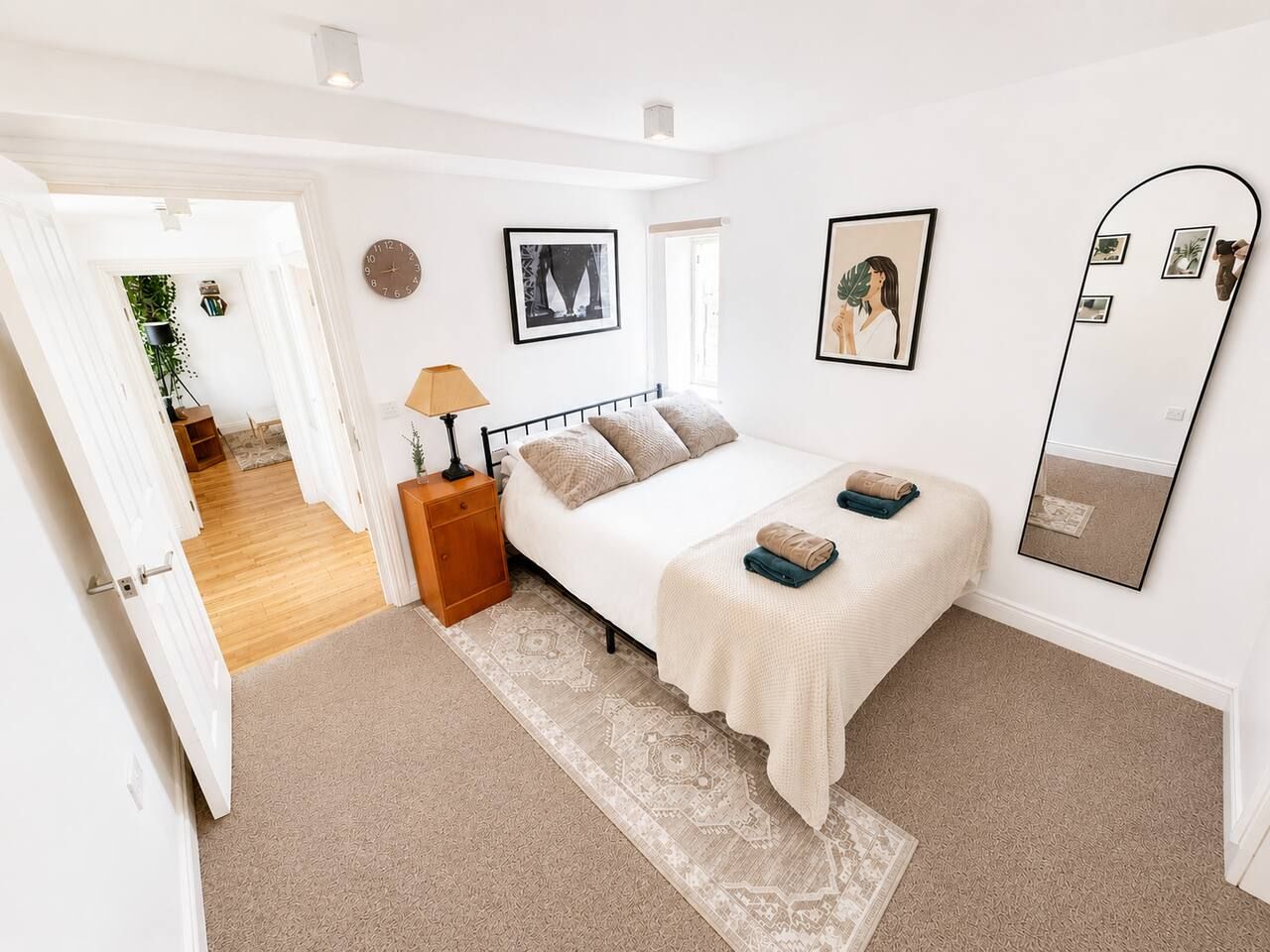 Een slaapkamer met een bed, nachtkastje, lamp en een grote spiegel.