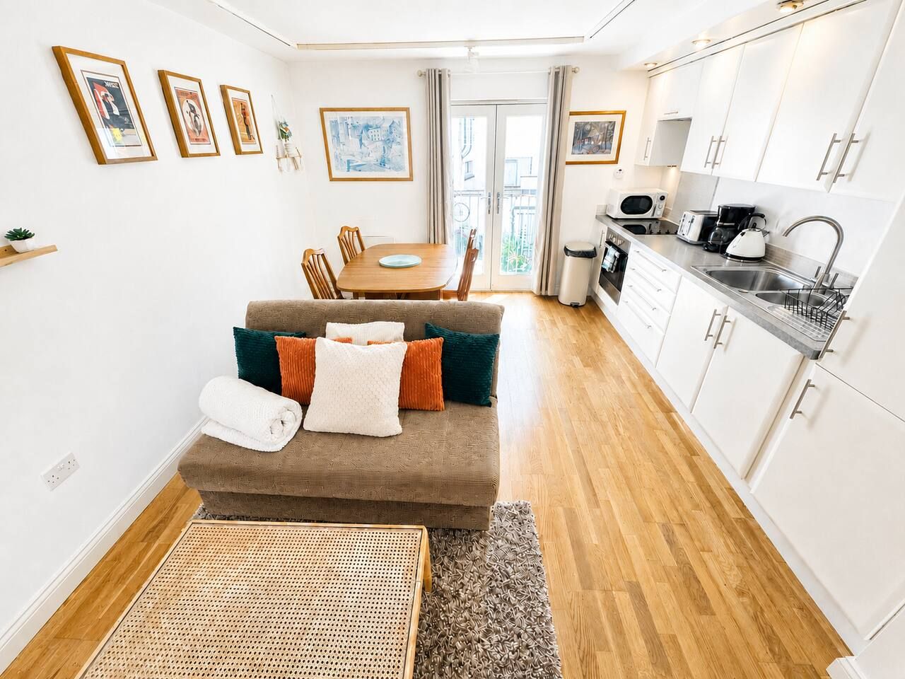Een knus woongedeelte met een bank, eettafel, kitchenette en uitzicht door een glazen deur.