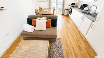 Een knus woongedeelte met een bank, eettafel, kitchenette en uitzicht door een glazen deur.