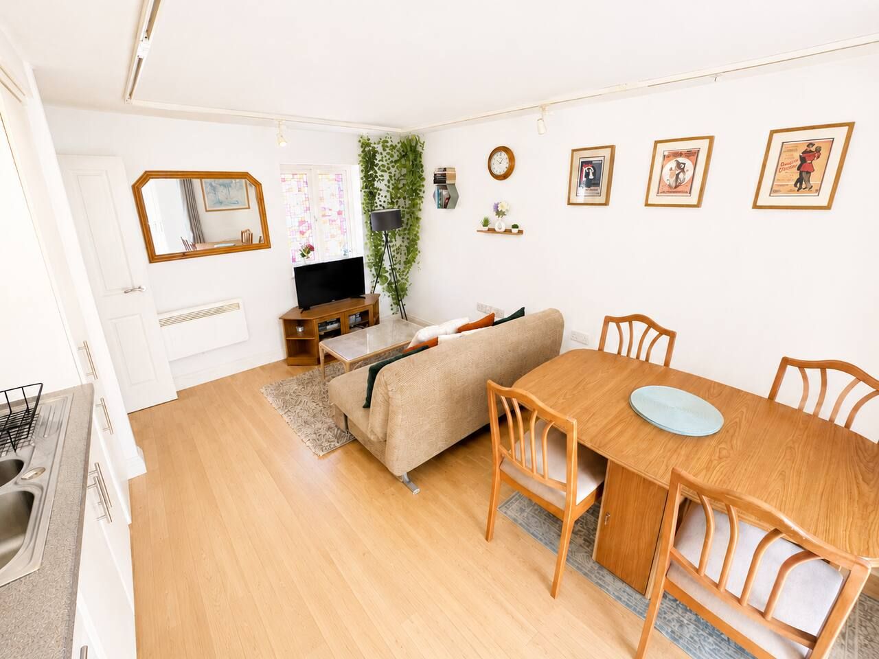 Een moderne woonkamer met een bank, eettafel, stoelen, een televisie en een plant.