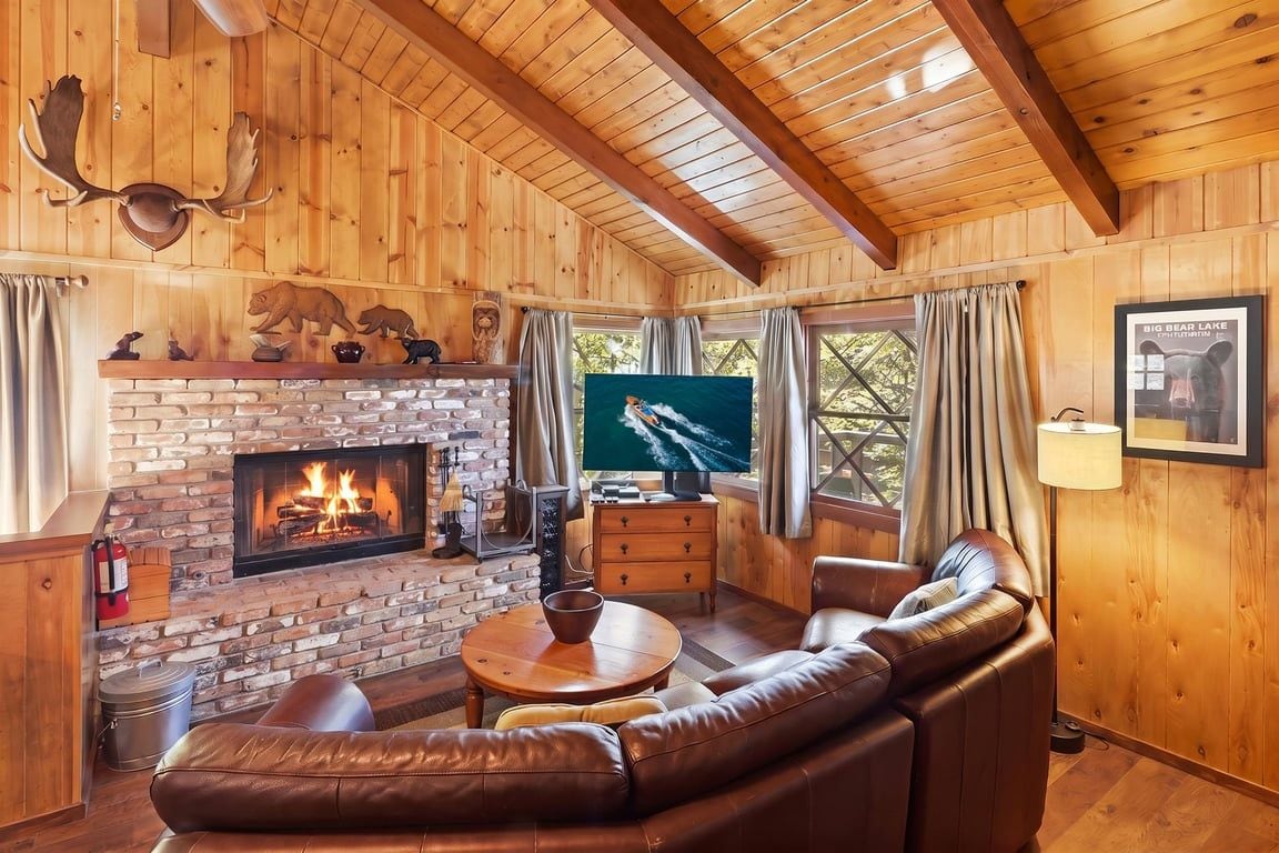 A cozy cabin interior with a fireplace, leather sofa, and a television.