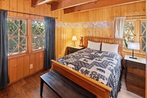 A wooden-paneled bedroom with a bed, bedside tables, and a bench. - PET FRIENDLY! Fenced Yard! Game Room! Flat Driveway! (Big Bear Lake)