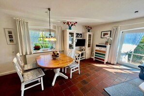 Ein Essbereich mit Holztisch und -stühlen, einem Fernseher, Schränken und einem fenster mit Vorhängen.