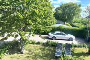 Eine Auffahrt mit einem geparkten Auto, einem Baum und einer Hecke.