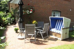 Eine Außenpatio mit Tisch und Stühlen, einer Rattansofa und einer Backsteinmauer im Hintergrund.