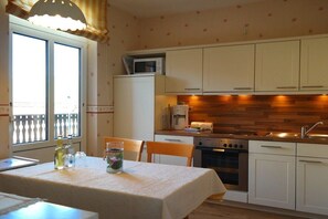 A kitchen with white cabinets, a wooden backsplash, a coffee machine, and a dining table with chairs. - Haus Hansen Wyk - Holiday Apartment 01 (Wyk)