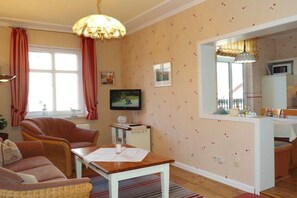 A cozy living room with a sofa, a dining table, and a television. - Haus Hansen Wyk - Holiday Apartment 01 (Wyk)