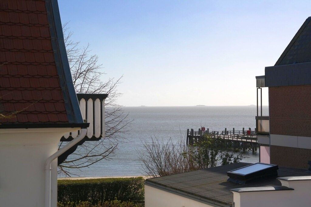 Une vue sur la côte, avec une jetée en bois s’étendant dans l’eau, un ciel dégagé et un bâtiment doté d’un toit en pente.