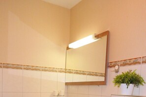 Ein Badezimmer mit Spiegel, Lampenleuchte und einer Topfpflanze.