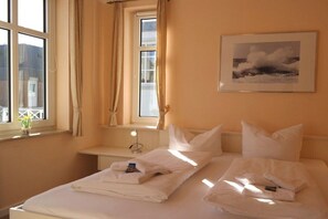 Ein Hotelzimmer mit zwei Betten, einem Fenster mit Vorhängen, einem Nachttisch mit Lampe und einem gerahmten Bild an der Wand.