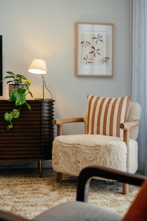 Een gezellige woonkamer met een houten stoel, een lamp, een potplant en een lijst met een foto aan de muur.