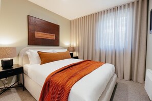 Een hotelkamer met een bed, nachtkastjes, een lamp, een schilderij en gordijnen.