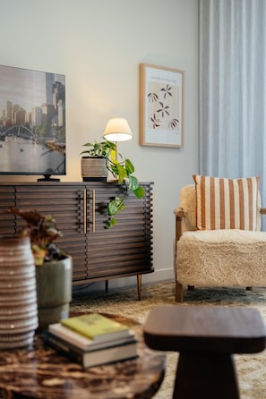 A modern living room with a flat-screen TV, a lamp, a striped armchair, and a decorative plant. - StayCentral - The Marque II - The Marque II - 2 Bedrooms, 2 Beds, 1 Bathroom, 2 Car Park (Collingwood)