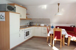 A compact kitchen with a microwave, stove, and sink, a dining table with chairs, and a red sofa. - Haus Hansen Wyk - Holiday Apartment 03 (Wyk)