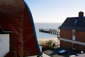 A coastal view with a pier extending into the sea, a building with a sloped roof, and a clear sky. - Haus Hansen Wyk - Holiday Apartment 03 (Wyk)