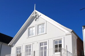 Ein weißes Gebäude mit einem Satteldach und einem Balkon mit Metallgeländer.