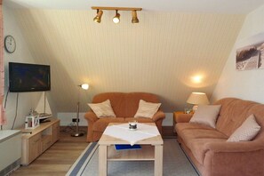 A cozy living room with a sofa, a coffee table, a lamp, and a television. - Haus Hansen Wyk - Holiday Apartment 03 (Wyk)