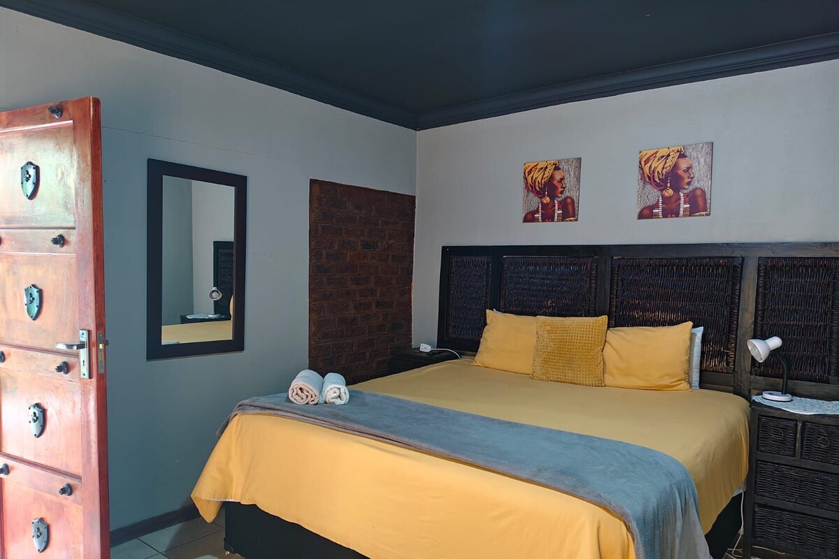 Une chambre à coucher avec un lit, une armoire en bois, un miroir et deux tableaux accrochés au mur.