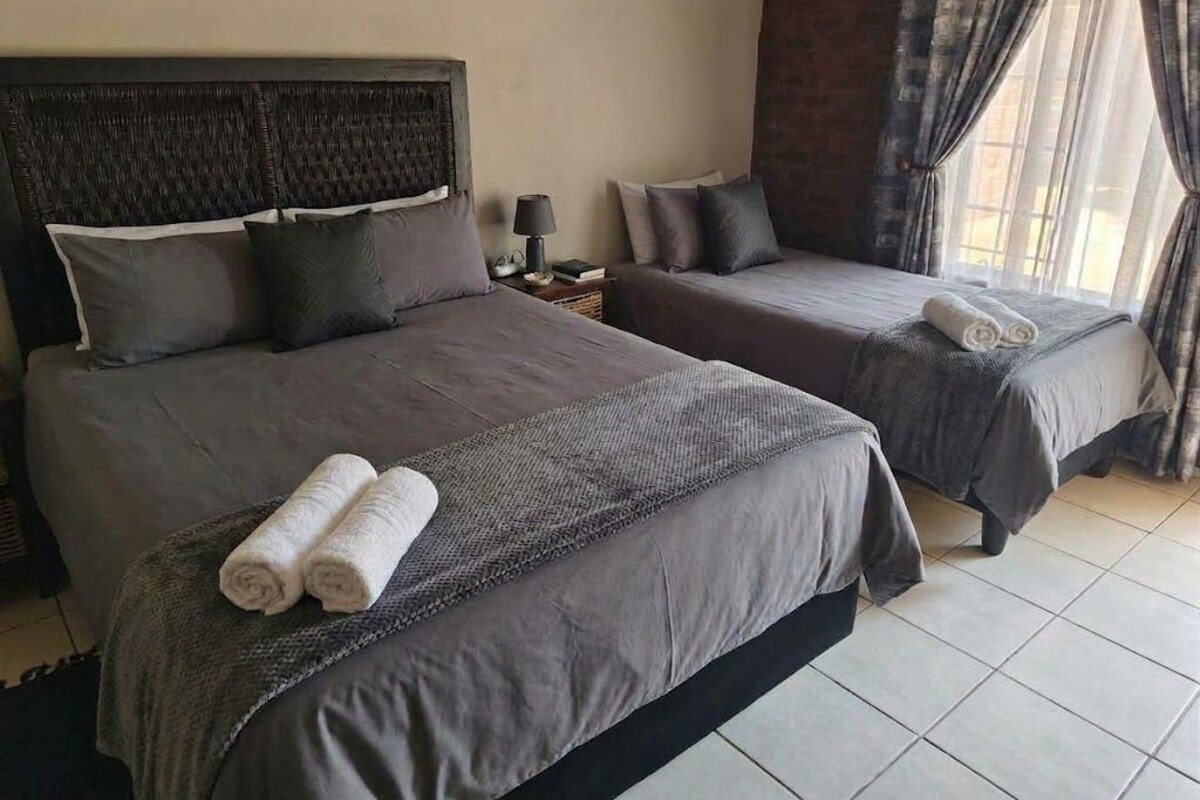 Une chambre d’hôtel avec deux lits, une table de chevet, une lampe et une fenêtre avec des rideaux.