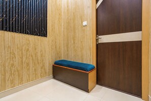 A corner of a room with a wooden bench, a door, and a wall with a vertical pattern. - OYO 827785 TJ INTERNATIONAL (Lucknow)