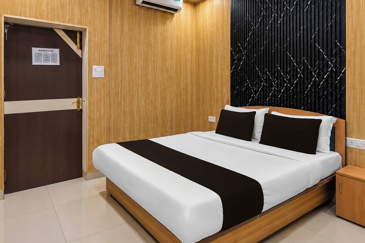 Una habitación de hotel con piso de madera, una cama con ropa de cama blanca y negra, una mesita de noche de madera, una pared texturizada negra y una puerta con un letrero.