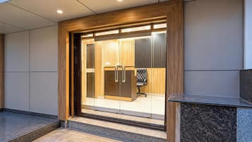 Una entrada de oficina moderna con puerta de vidrio, marco de madera y una silla de oficina negra en el interior.
