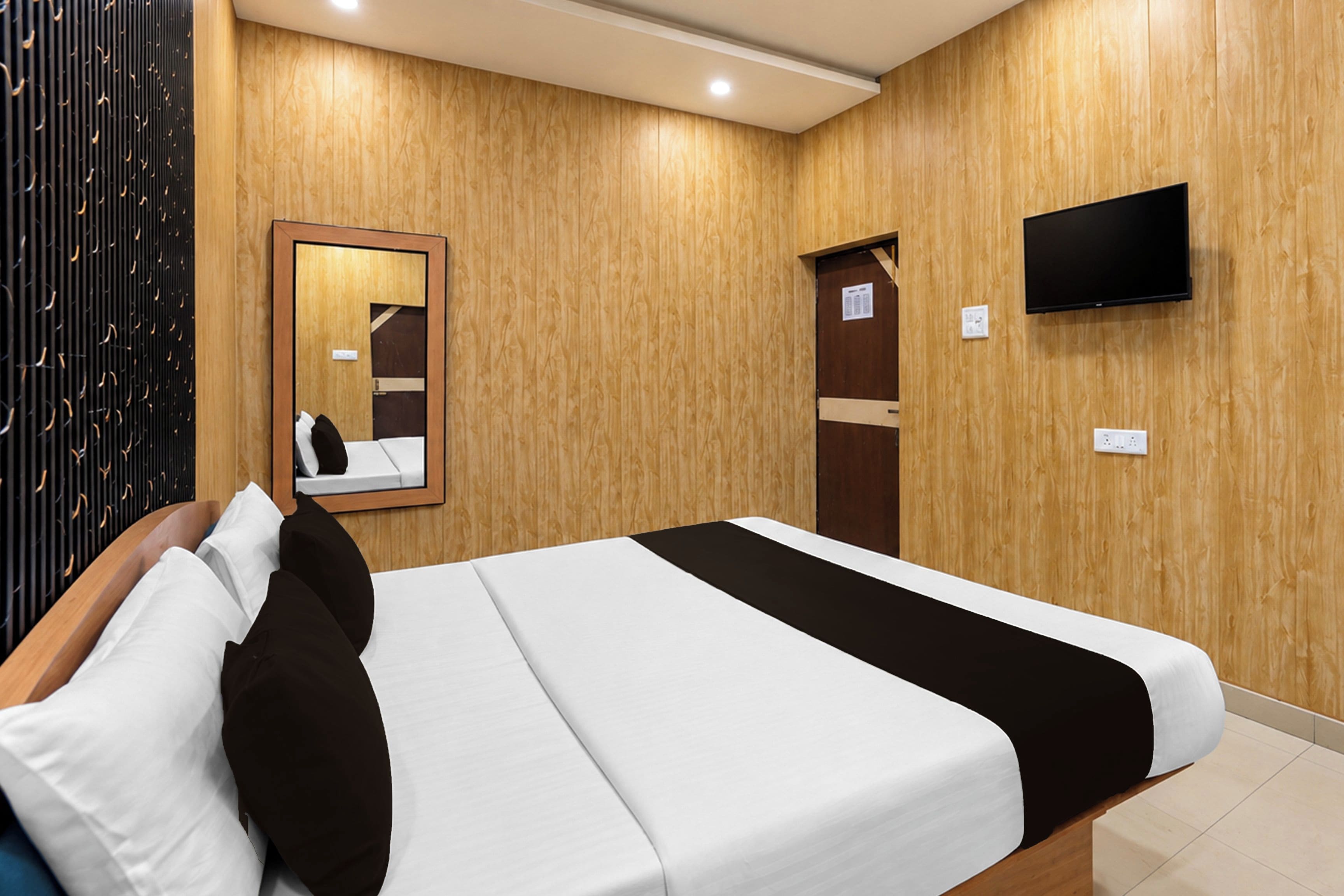 Habitación de hotel con cama, televisor de pantalla plana montado en la pared y panel de pared de madera.