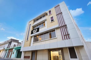 Un hôtel à la façade moderne, avec une enseigne bien visible indiquant qu’il fait partie du groupe OYO, et un ciel dégagé en arrière-plan.