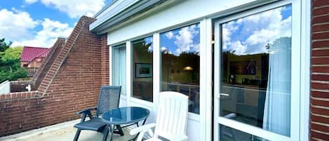 Een terras met een bakstenen muur, een glazen deur en twee stoelen.