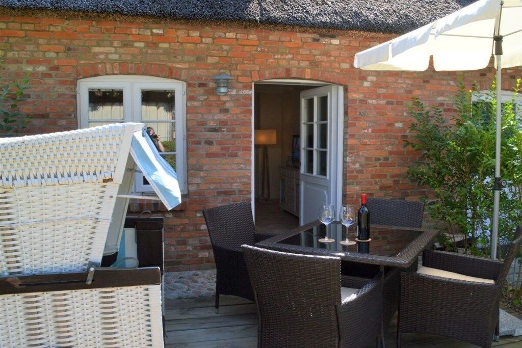 Un bâtiment en briques avec une table et des chaises en verre, un parasol blanc et une bouteille de vin.