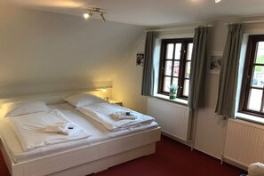 A hotel room with a large bed, two bedside tables, a window with curtains, and a radiator. - Hansen Nieblum - Holiday Apartment 1 (Nieblum)