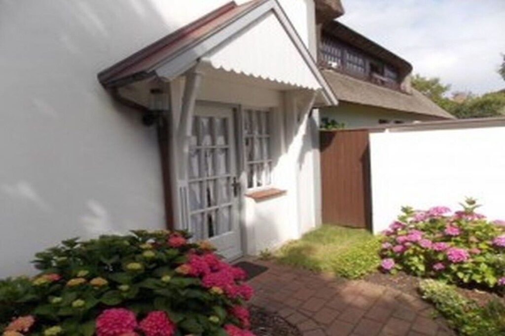 A white building with a brown roof, a wooden fence, and a brick pathway.