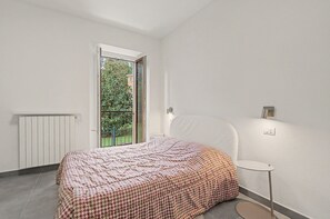 Un dormitorio con cama, una mesita, un radiador y una ventana con vistas a zonas verdes.