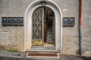 Una entrada arqueada con una reja de metal, varios escalones que llevan a una puerta y buzones a ambos lados.