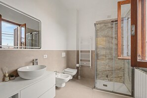 A modern bathroom with a large mirror, a vessel sink, a toilet, a bidet, and a glass-enclosed shower.