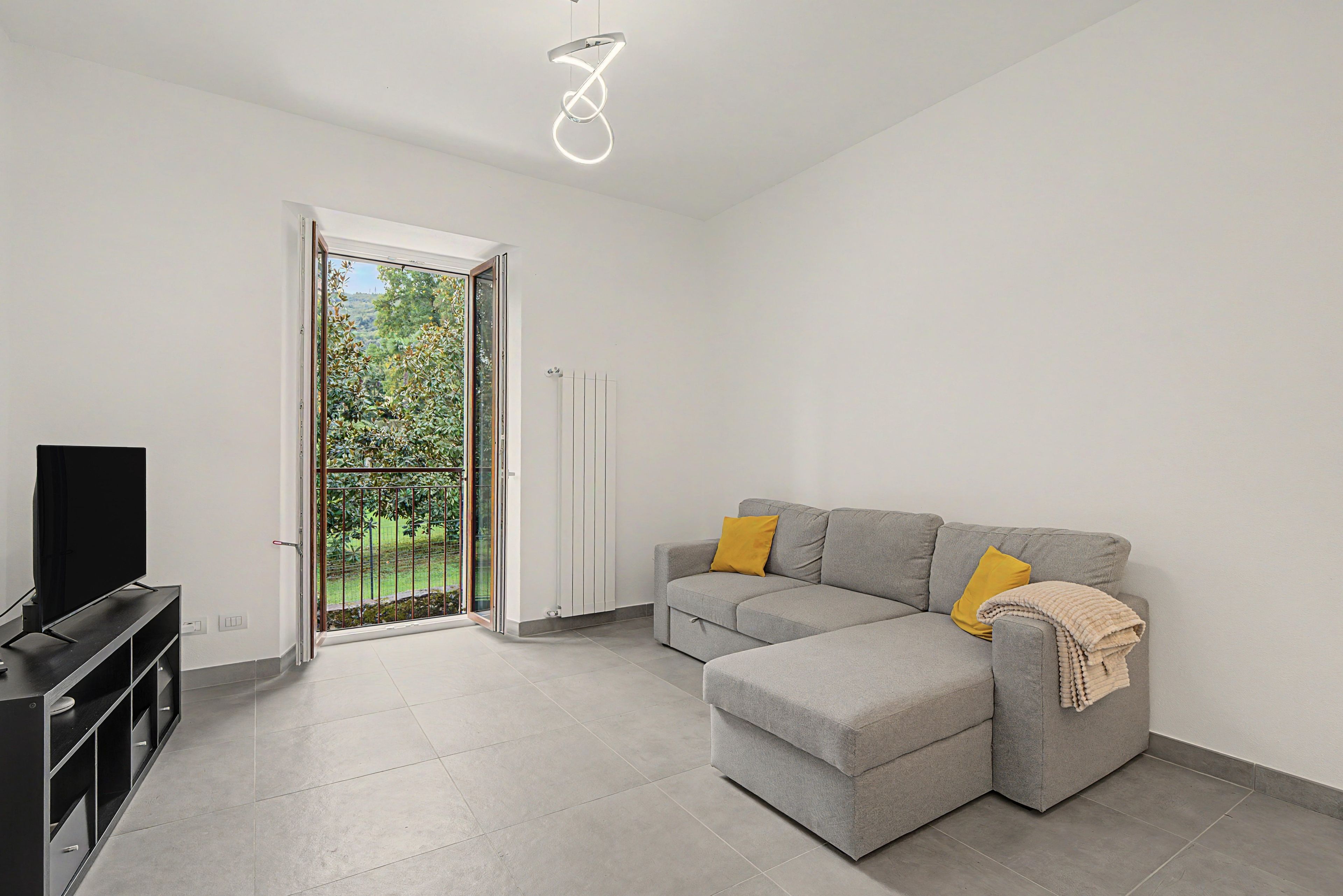 Un salon moderne avec un canapé d’angle gris, un téléviseur à écran plat et une porte-fenêtre coulissante donnant sur un balcon.