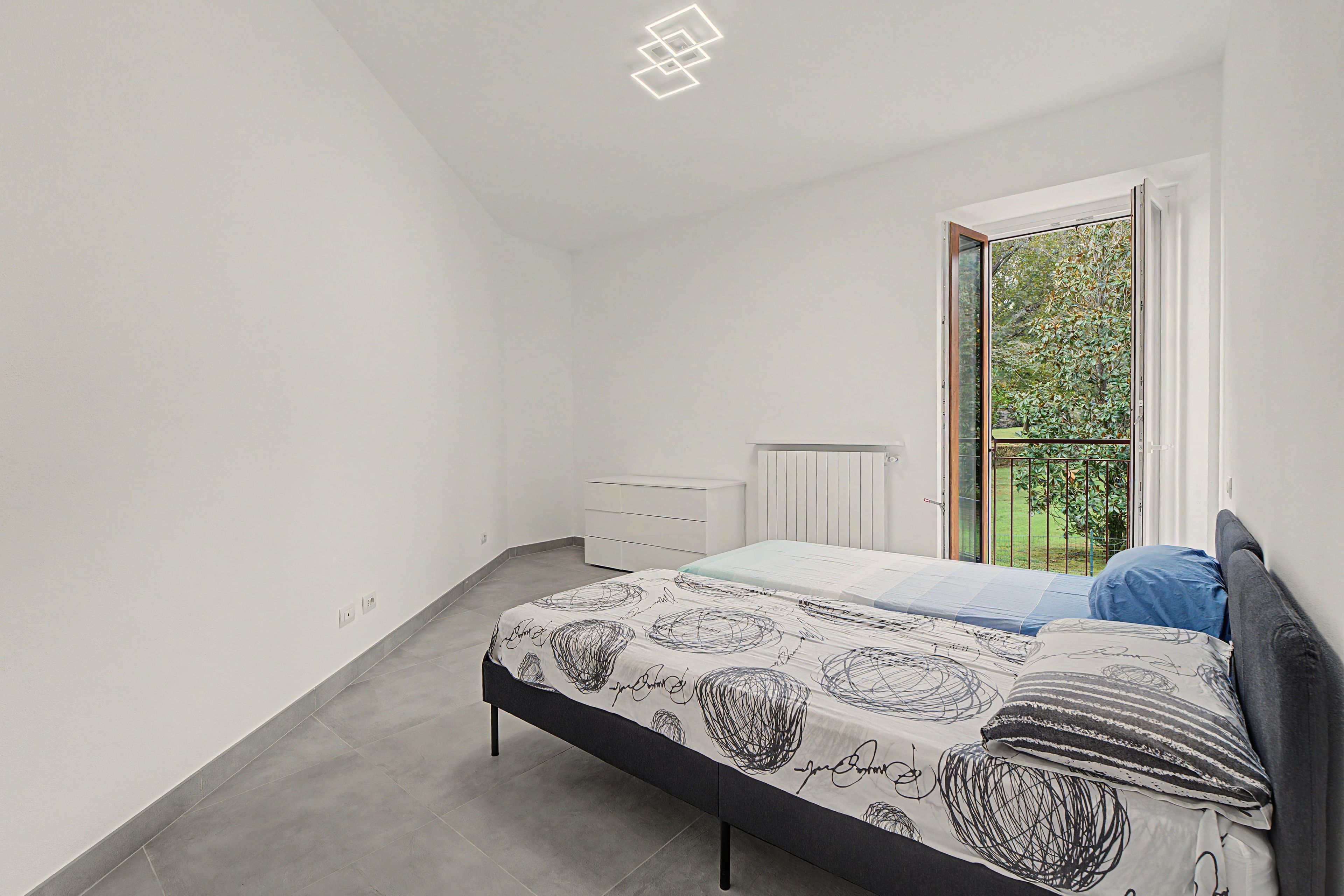 Une chambre à coucher comprenant un lit, une commode, un radiateur et une fenêtre donnant sur un paysage verdoyant.