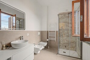 Un bagno moderno con uno specchio grande, un lavabo a incasso, un water, un bidet e una doccia con pareti in vetro.