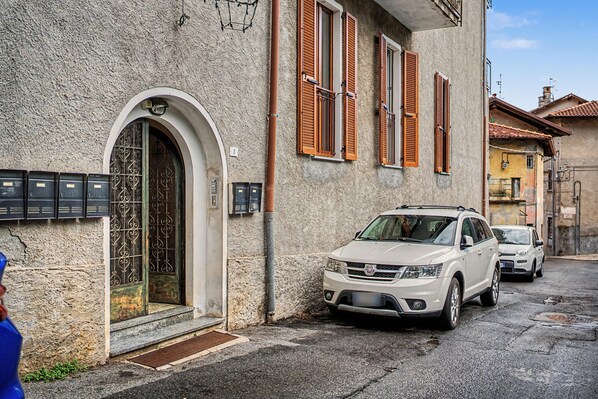 Un SUV blanco estacionado frente a un edificio con fachada de piedra, contraventanas de madera y una reja de metal.