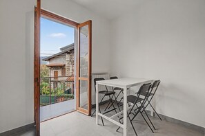 Un piccolo balcone con tavolo e sedie, vista su un edificio con facciata in pietra e cielo sereno.