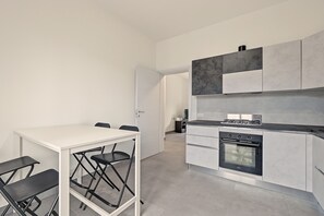 A modern kitchen with a gas stove, oven, and white cabinetry. There is a dining table with chairs and a small black cabinet. - Holiday home 'Maison Du Lac' with balcony and Wi-Fi (Baveno)