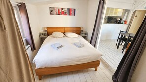 A bedroom with a wooden bed, white linens, and a view of a dining area. - The sea breeze, ocean views, and direct access to the beach (Saint-Côme-de-Fresné)