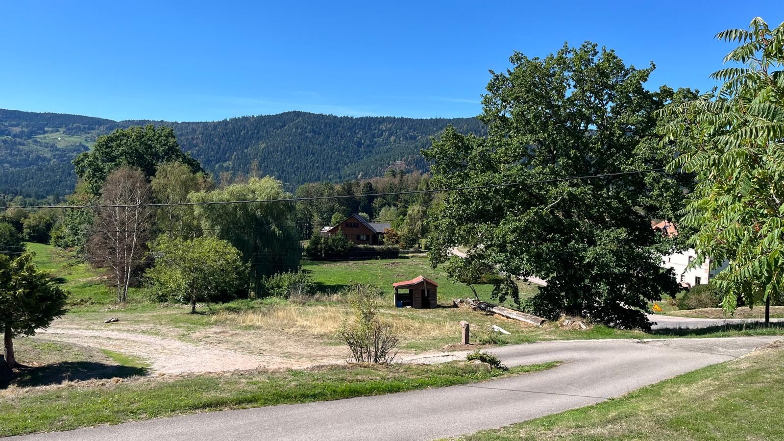 A rural road with a small building and trees on the side.