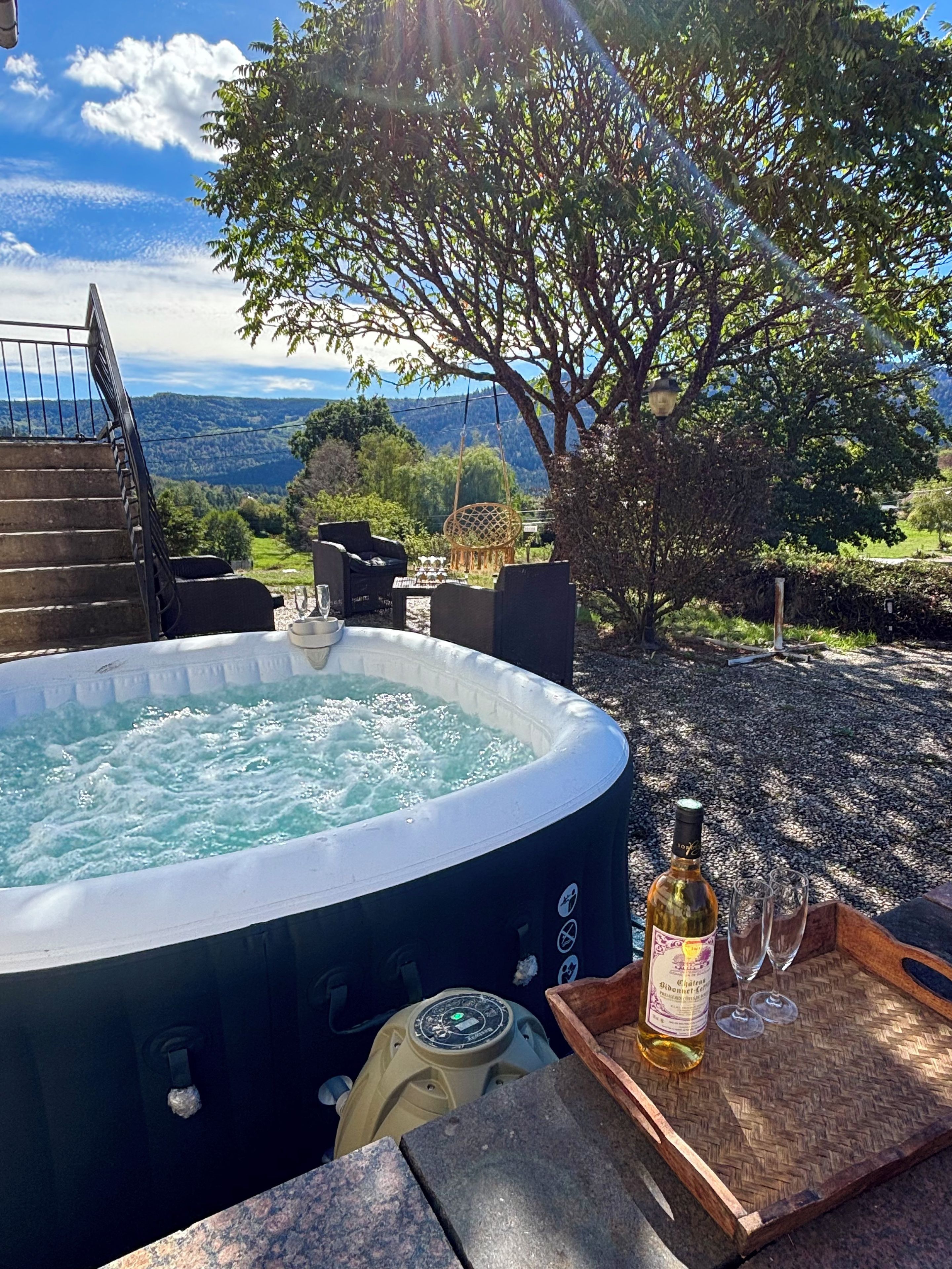 Un bain à remous avec vue sur le paysage, une bouteille de vin et des verres sur un plateau en bois.