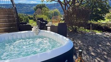 Un bain à remous avec vue sur le paysage, une bouteille de vin et des verres sur un plateau en bois.